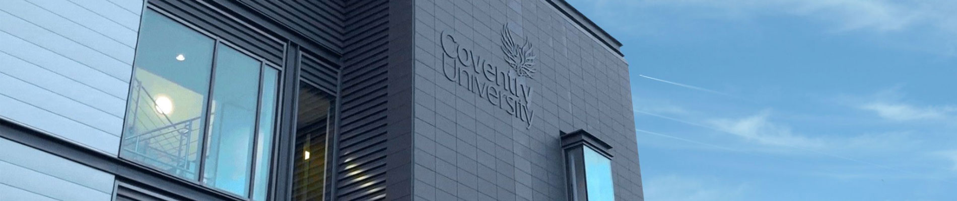 A close up of the Coventry University logo on the NITE building, against a blue sky.
