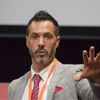 Andy David in a grey suit, speaking at an event