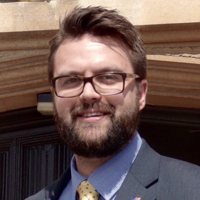 Headshot of Matthew Tragheim outside in a suit.