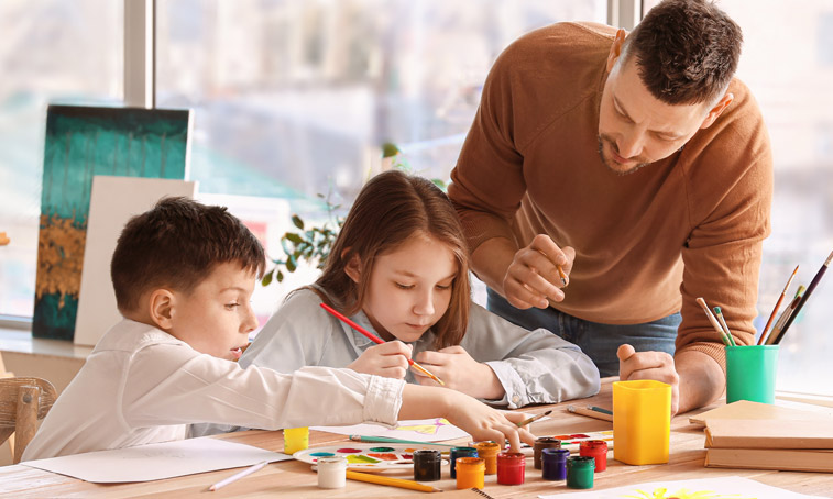 A young male teacher painting with young students in a classroom.