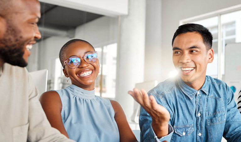 Teachers in a classroom sitting around a laptop talking.