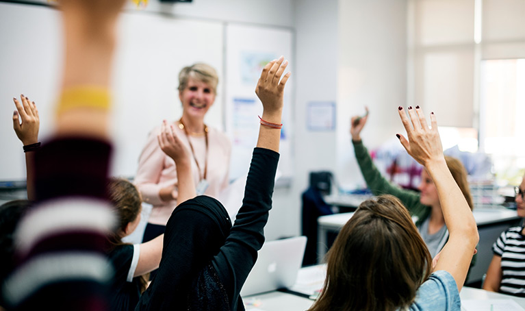 Teacher standing at the front of the classroom with students arms in the air