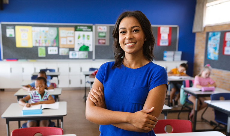A female teacher with arms crossed smiling in a classroom.