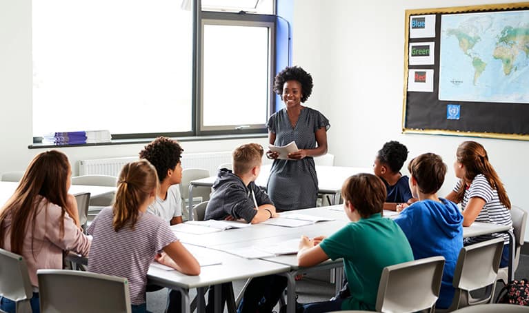 Teacher stood at the front of a classroom with young students looking towards her
