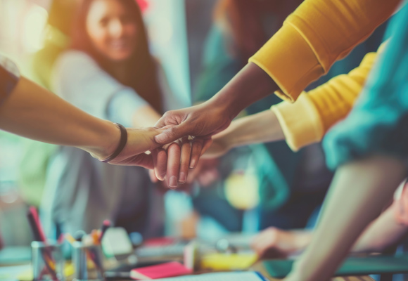 Teachers with their hands on top of each other above a classroom table of paints.