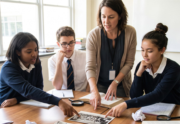 Secondary school students and their teacher collaborating on a history project while analysing old photographs around a classroom table