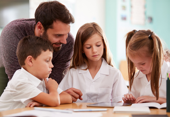 A male teacher with young students working around a table.