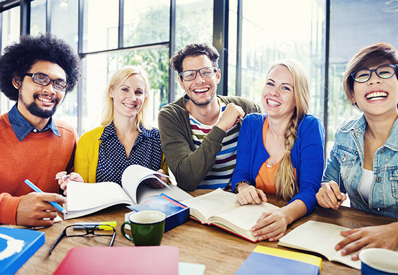 Five diverse adults in colourful tops sat at a table smiling at the camera.