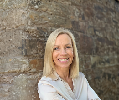 Claire Amed leaning against a wall with her arms crossed, smiling at the camera