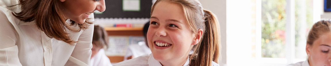Female teacher talking to pupil sat at desk.