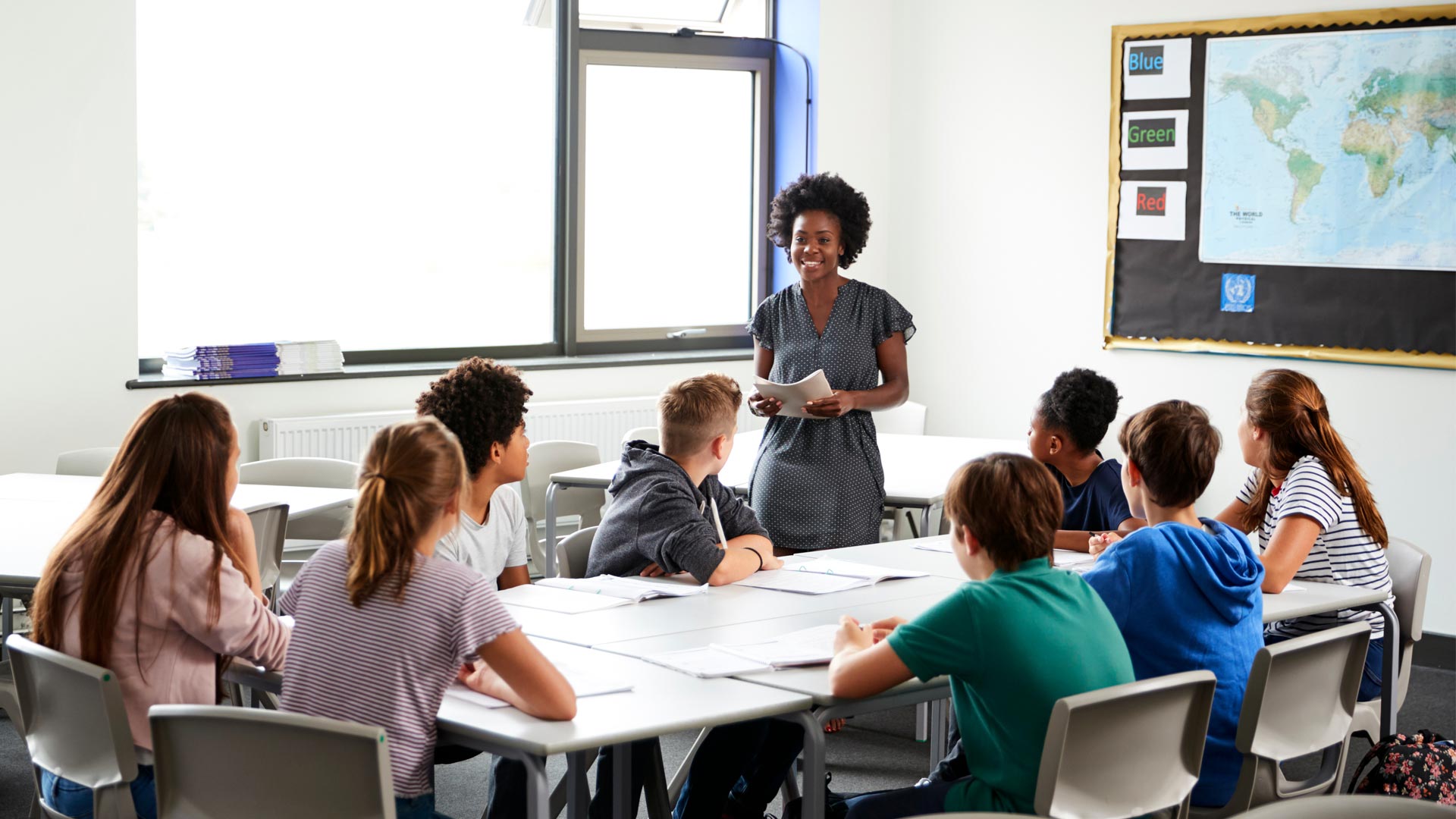 A teacher stood in front of a group of students sat around a large table.