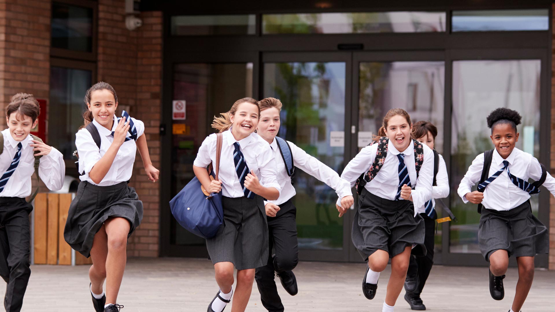 A group of mixed gender and ethnicity high school children running and laughing together.