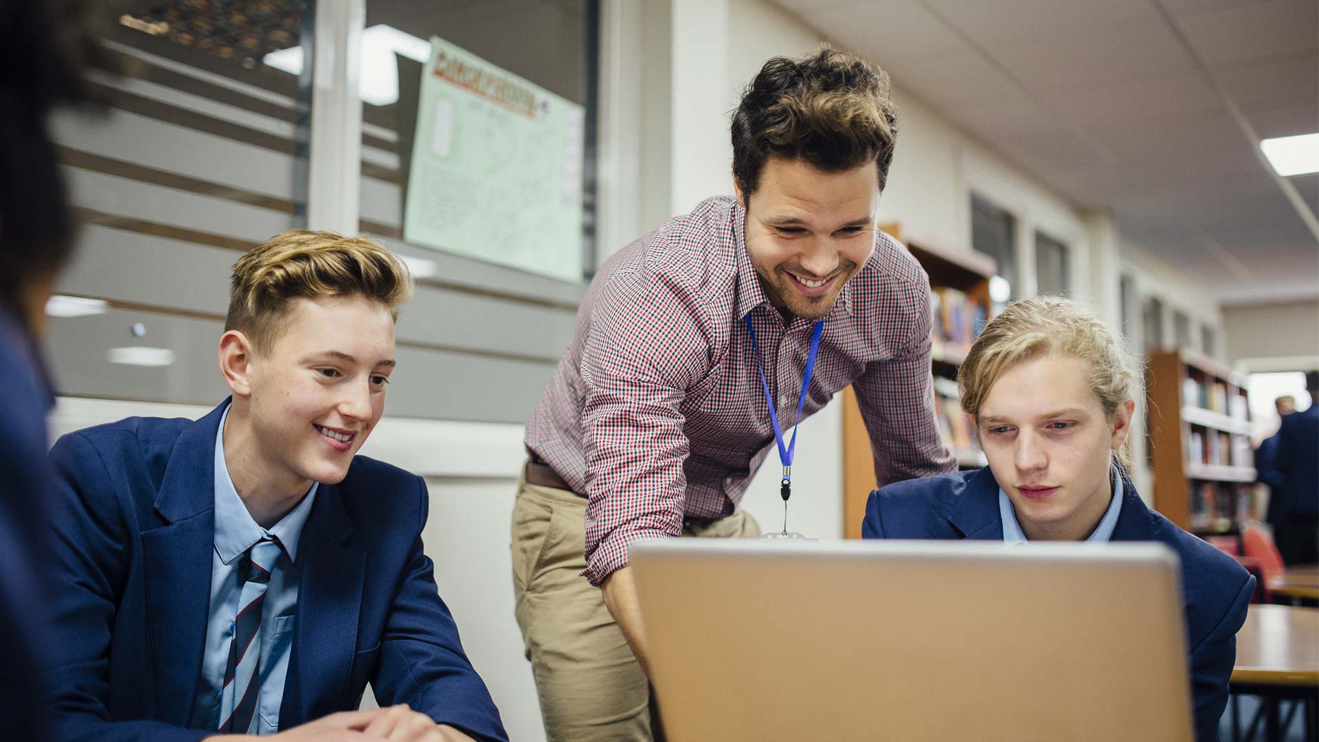 A male teacher helping a student using a laptop.