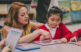 A teacher helping a young primary-aged child use a tablet.