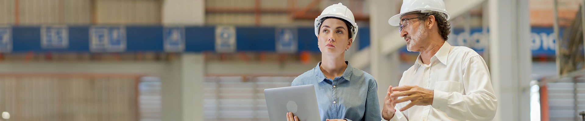 man and woman wearing hard hats looking around a warehouse