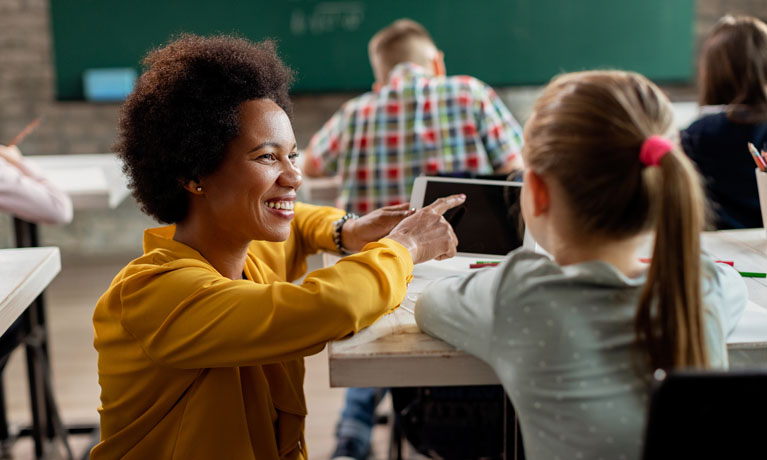 Teacher kneeling down at a desk helping a student