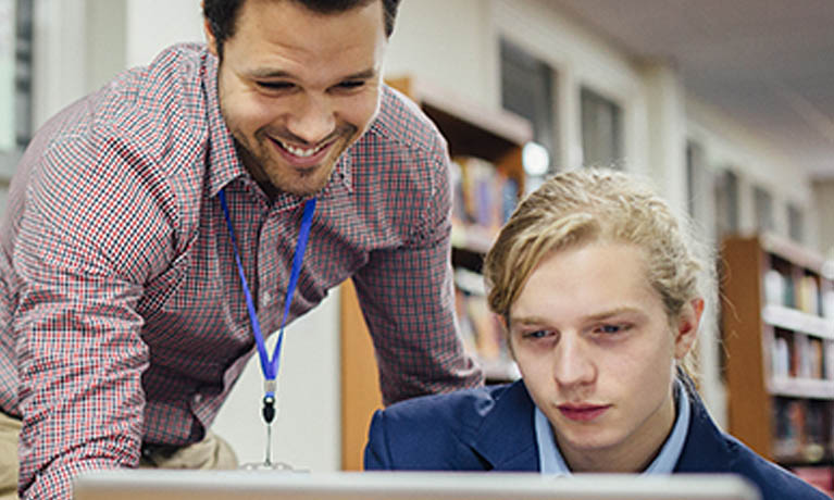 teacher helping a pupil looking at laptop