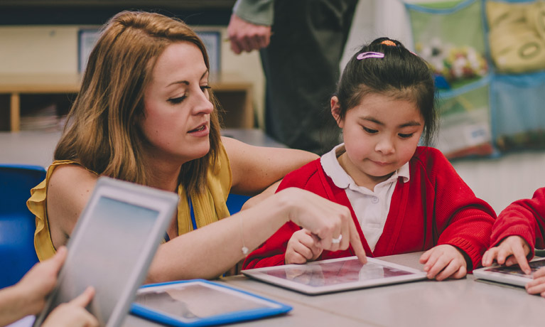 A teacher helping a young student work on a tablet.