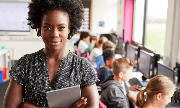Female teacher with pupils working on computers in the background.