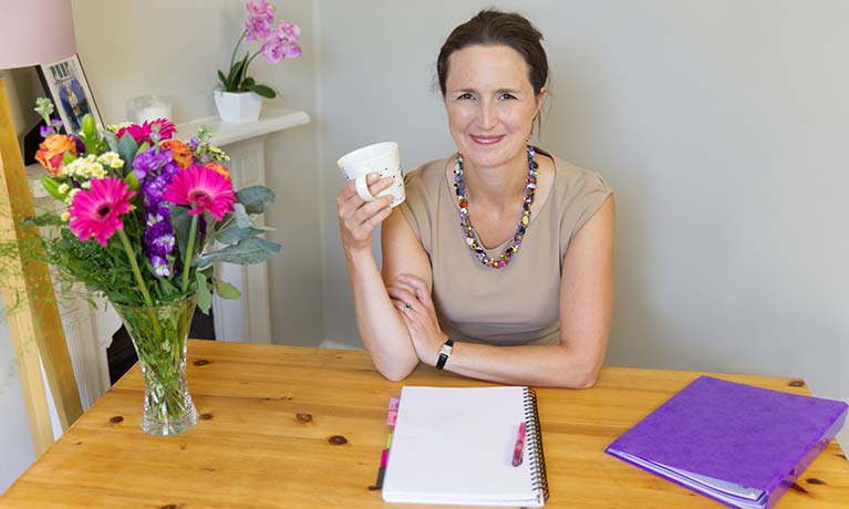 Lucinda Powell sitting at a table with a notebook in front from her 