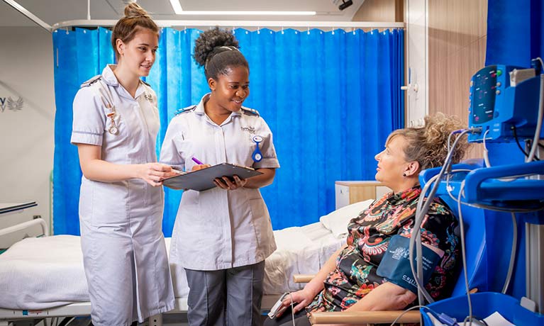 two young nurses talking to a patient in a mock hospital ward 