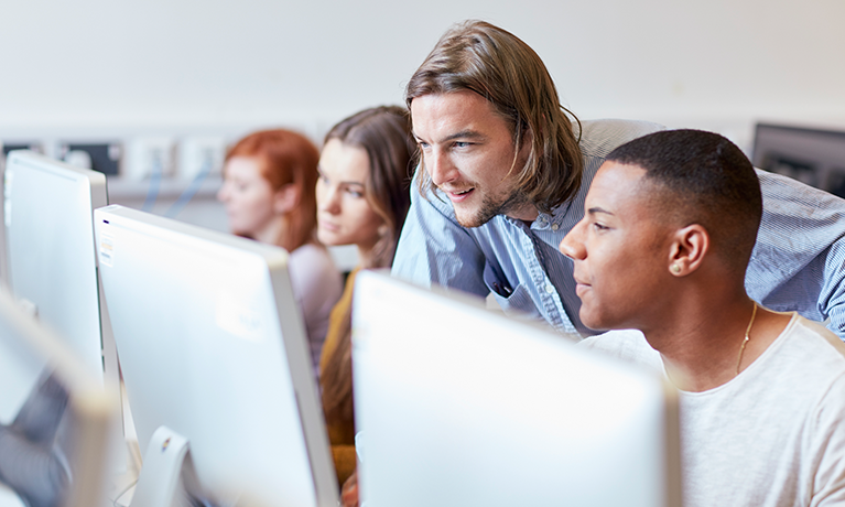 A teacher helping students sat at a computer