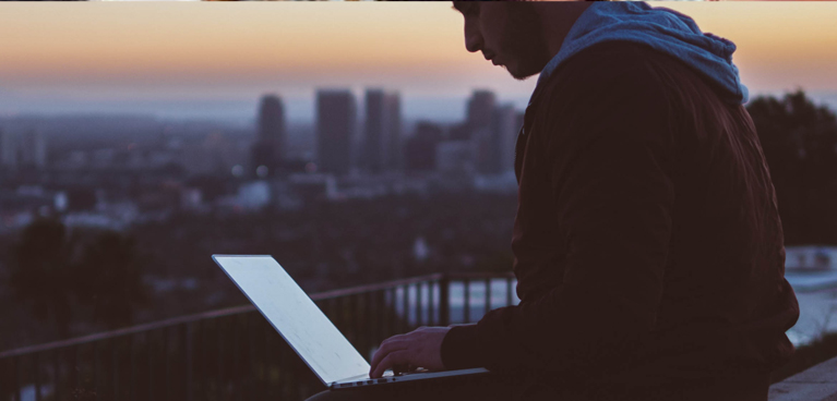 Young man in a rooftop working on a laptop at sunset.