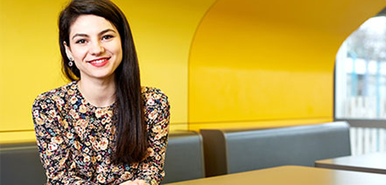 Student smiling and facing the camera against a yellow wall background 