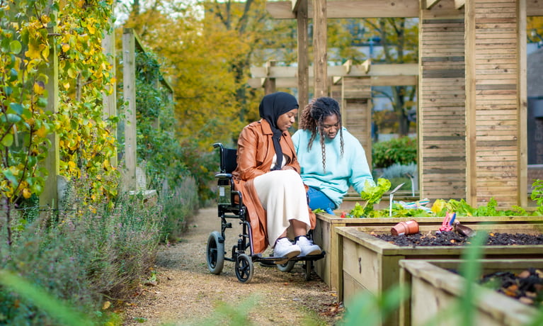 Member of a staff helping a lady in a wheelchair pick flowers