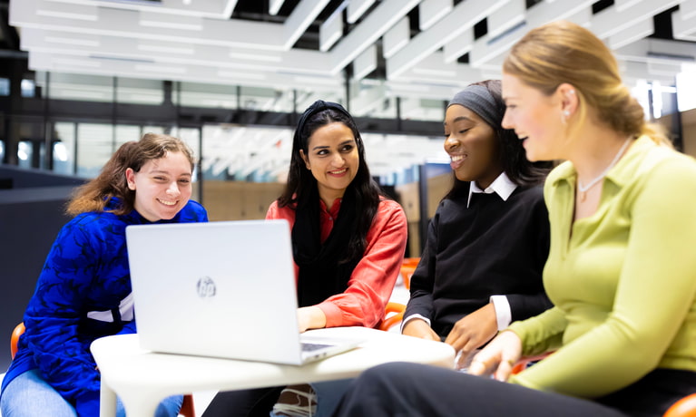 four students sitting around the table and looking on computer happily