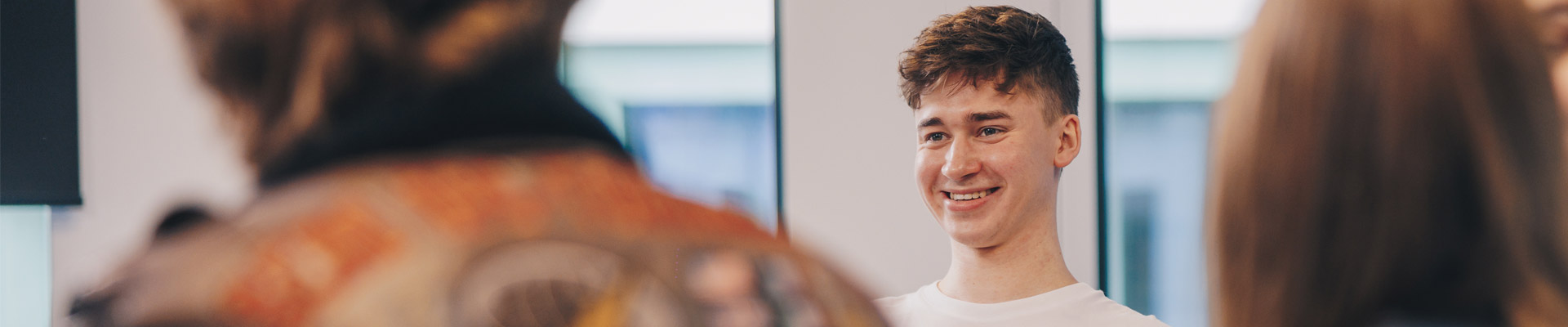 A student smiling while sat with other students on campus at Coventry University Wrocław.