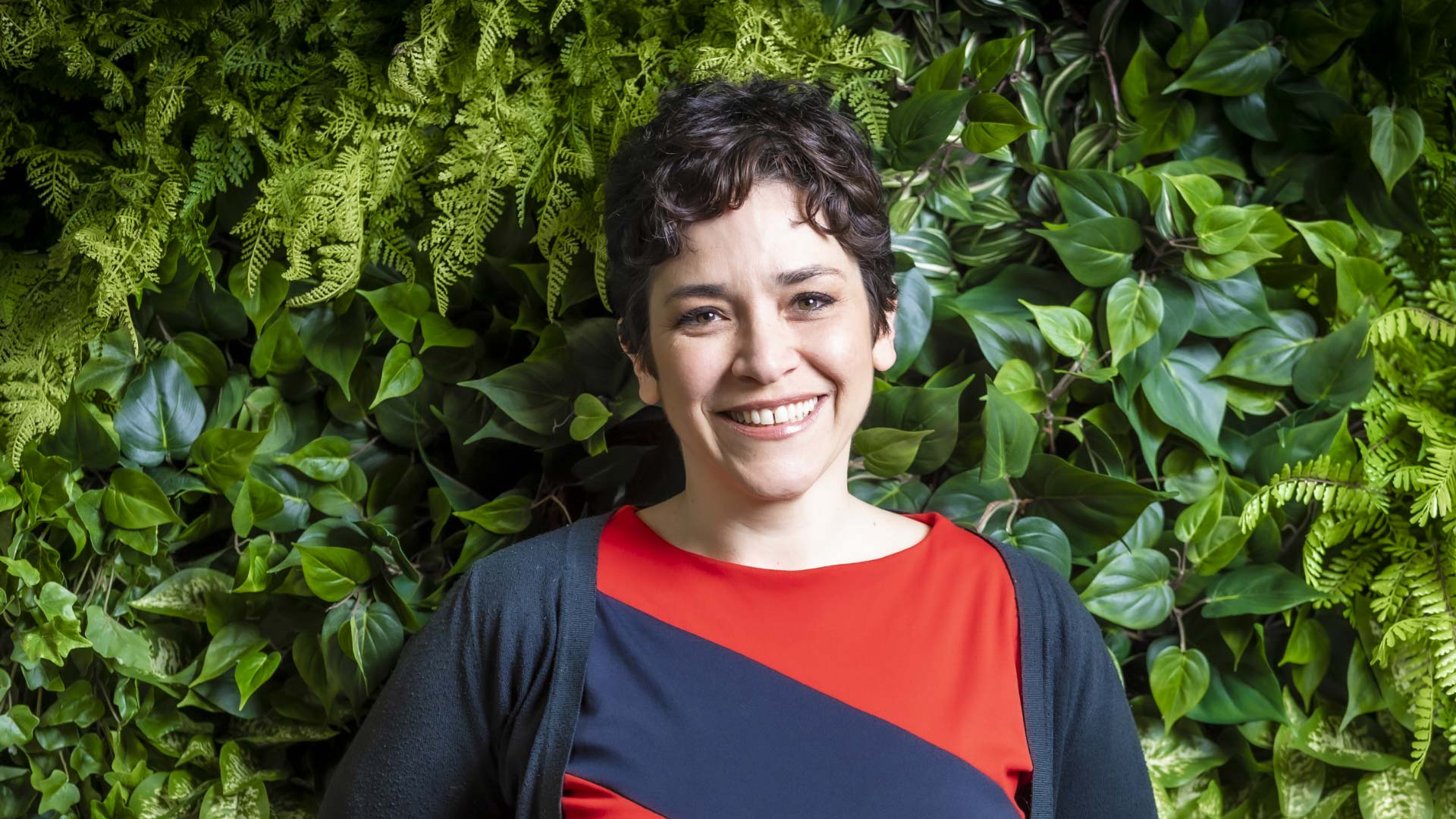 Woman standing smiling against a hedge