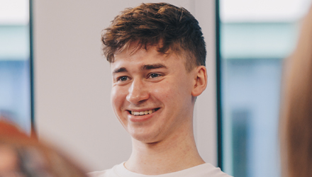 A male student smiling and sitting with other students.