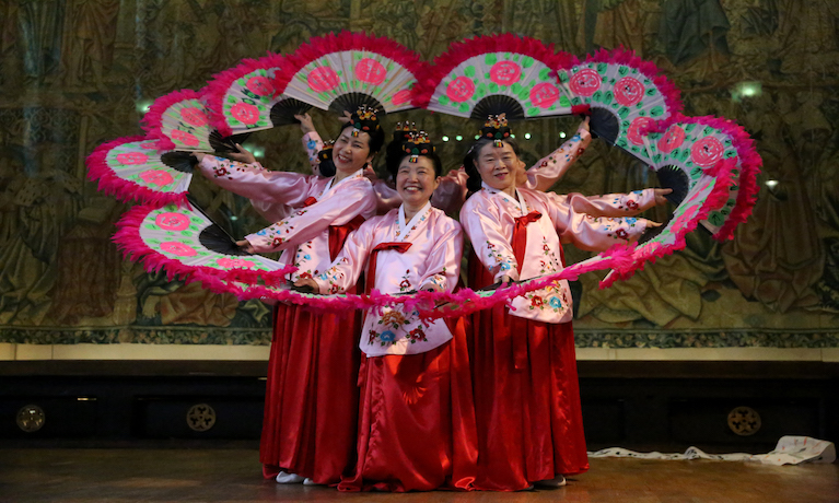 Korean female dancers in traditional dress forming a circle with fans.