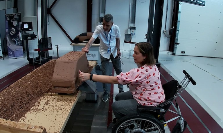 photo a woman in a wheelchair touching the clay model of a car.