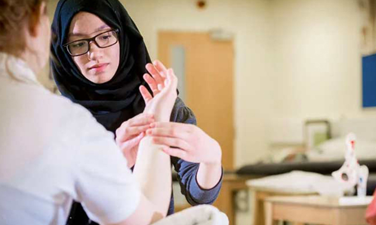 Physiotherapist student practicing in a class room on a students arm